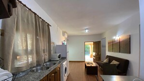 Cocina compacta con lavadora, microondas y lavaplatos. Cuenta con un comedor con mesa y sofá.