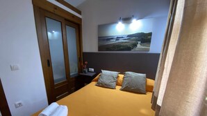 Une chambre d’hôtel avec un lit, une table de chevet, un miroir et un tableau représentant une scène de plage.