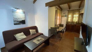 Un salon chaleureux avec un canapé marron, une table basse et une table à manger avec des chaises. Il y a également un coin cuisine avec un réfrigérateur et un téléviseur fixé au mur.