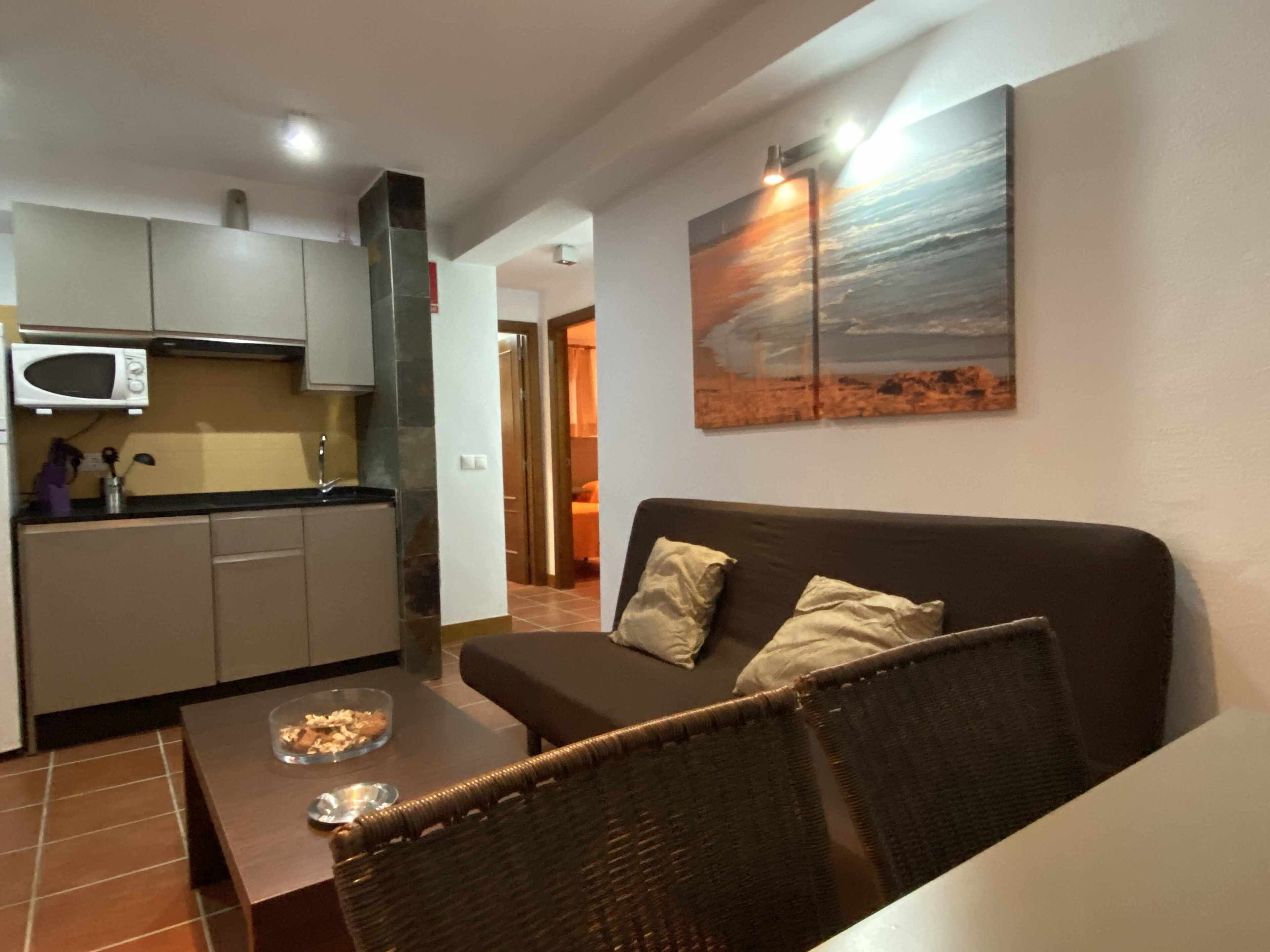 A living room with a brown sofa, a coffee table, and a kitchen area with a microwave.
