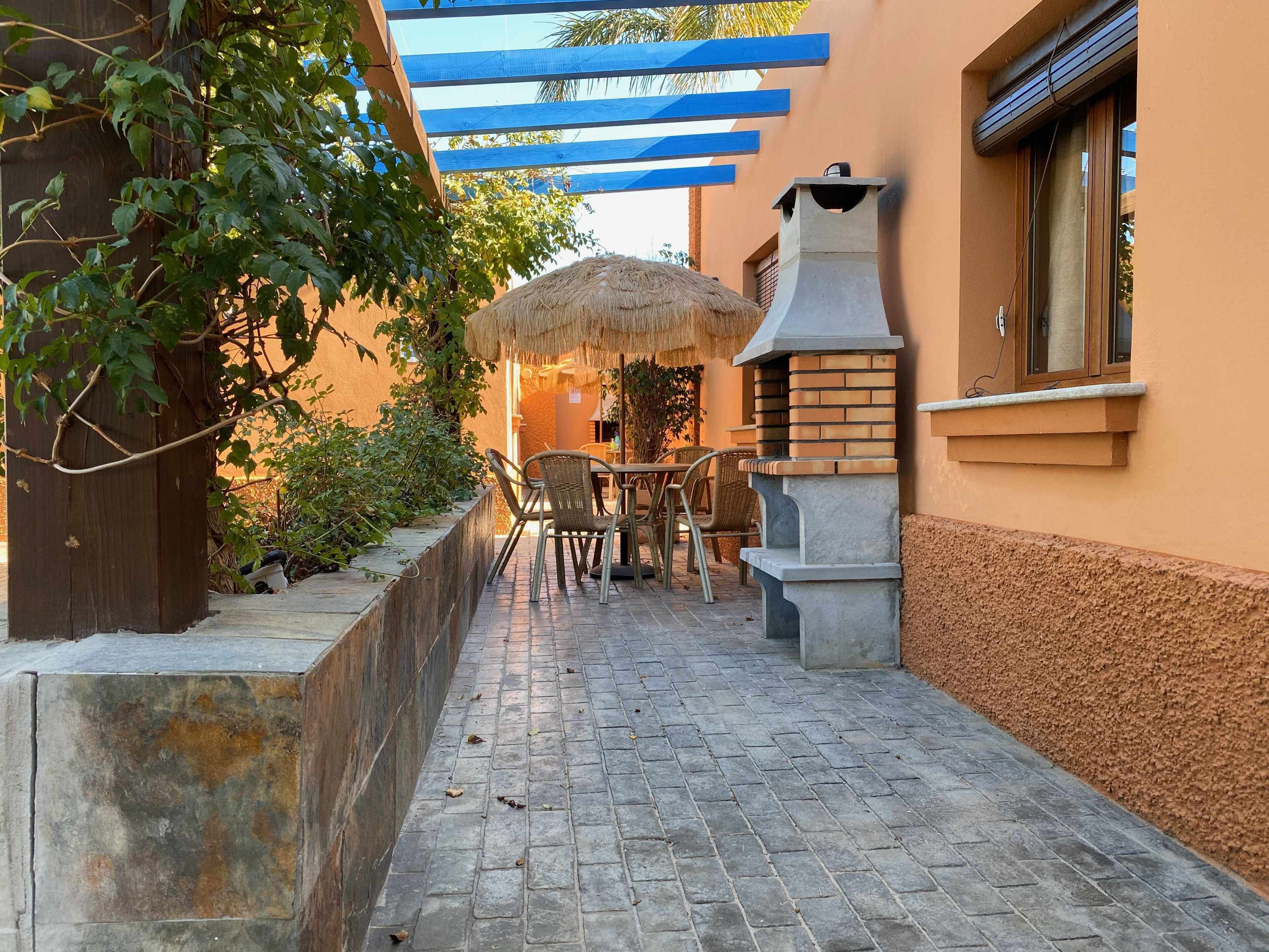A courtyard with a brick pathway, outdoor seating, a thatched umbrella, and a stone barbecue grill.