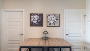 Ein Zimmer mit Holztisch und Bänken, zwei gerahmte Blumenbilder an der Wand und einer kleinen Metalltablett mit Kerzenhalter.