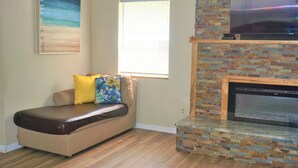 A living room with a beige sofa, a fireplace, a television, and a painting on the wall. - Riverside Island Bungalow (Daytona Beach)