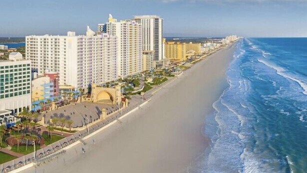 A coastal cityscape with high-rise buildings, a sandy beach, and a clear blue sky. - Riverside Island Bungalow (Daytona Beach)