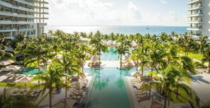 Un resort con piscina central rodeada de palmeras y sillones de descanso, con vista al océano.