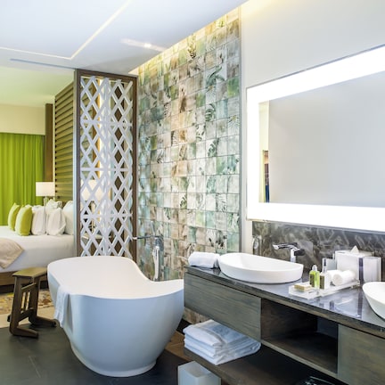 A modern hotel room with a large bed, a bathtub, and a vanity with two sinks.