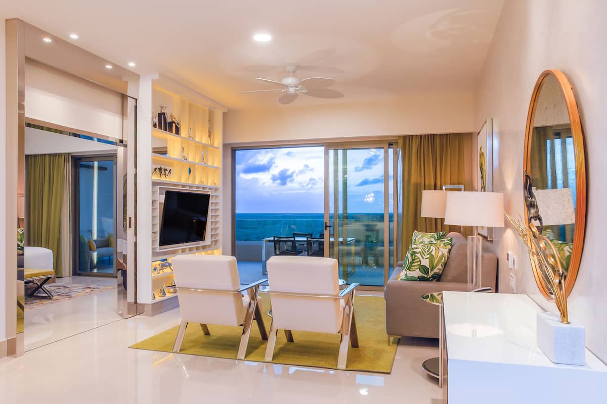 Una habitación de hotel moderna con balcón, televisión de pantalla plana, mobiliario blanco y un espejo grande.