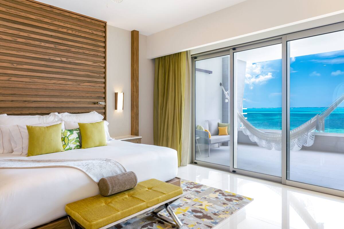 Habitación de hotel con una cama grande, vista al océano y una hamaca en el balcón.