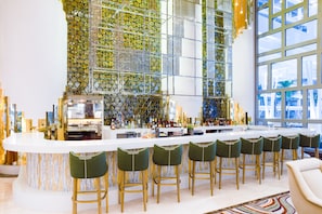 A modern bar with a white countertop, green bar stools, and a decorative glass wall.