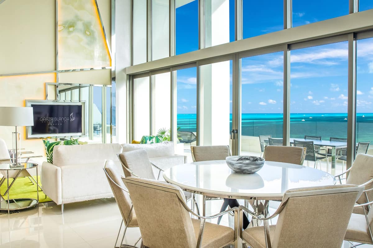 Una habitación de hotel moderna con un balcón amplio, una mesa de comedor redonda y una televisión.