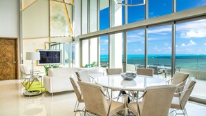 A modern dining area with a large glass table and chairs, a television, and a view of the ocean. - Garza Blanca Resort & Spa Cancun (Punta Sam)