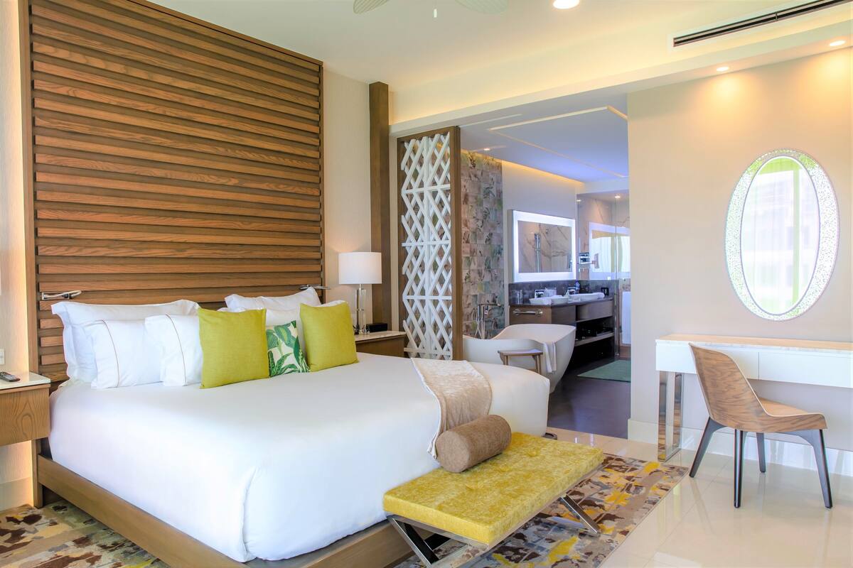 Una habitación de hotel moderna con una cama grande, un escritorio y un baño visible a través de una puerta abierta.