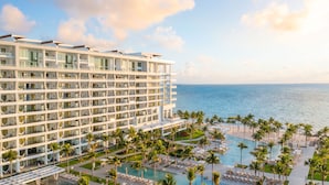 A modern hotel with multiple floors, a pool area with lounge chairs, and a view of the ocean. - Garza Blanca Resort & Spa Cancun (Punta Sam)