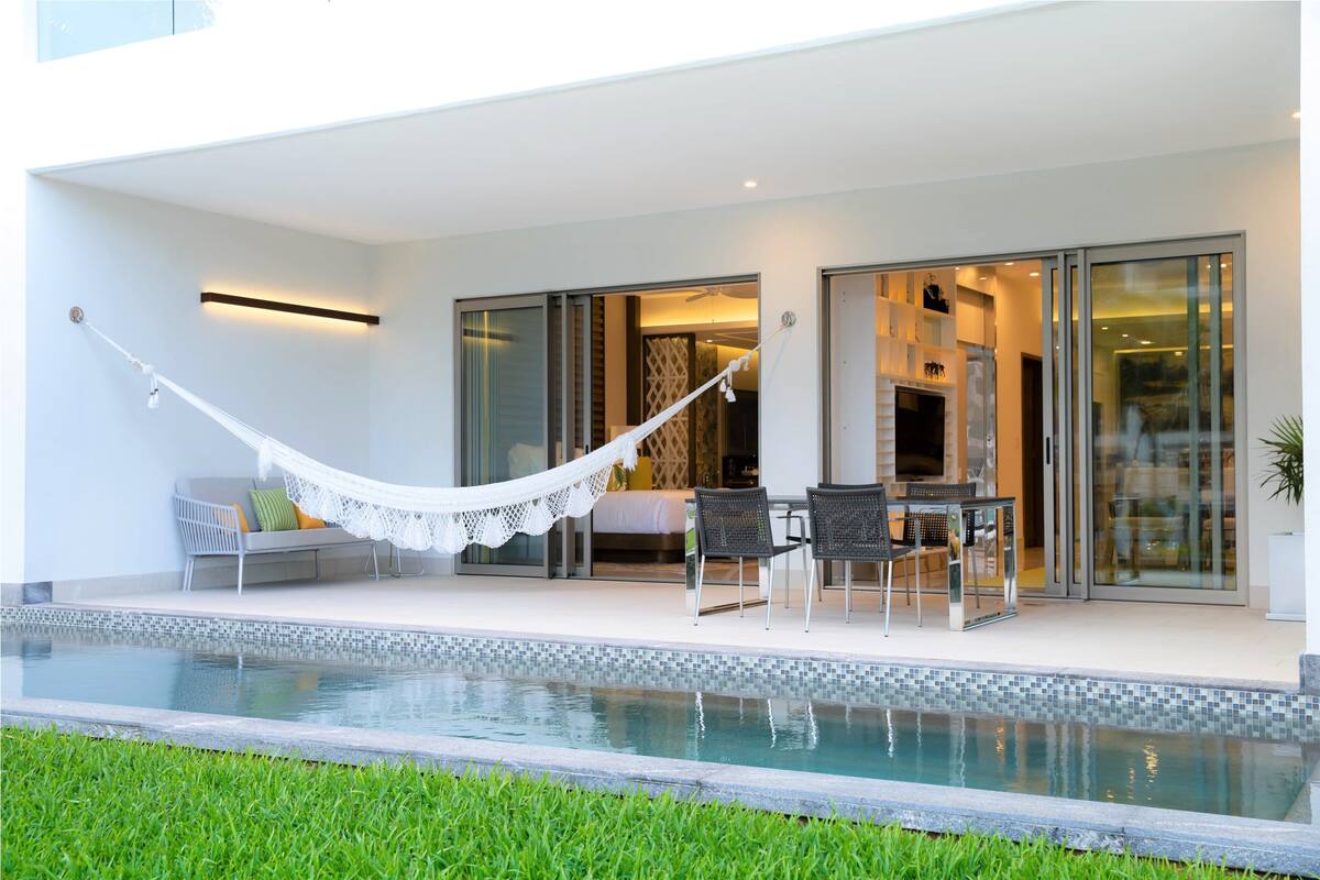 Un área de piscina moderna al aire libre con una hamaca, asientos y una zona de comedor.