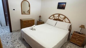 Un dormitorio con cama, cómoda, mesita de noche, lámpara, espejo y un cuadro en la pared.