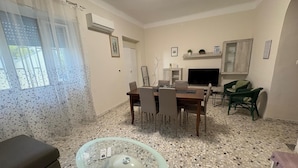 Un comedor con una mesa, sillas, una mesa de centro de vidrio, un sofá y un televisor.