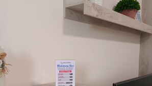 Un escritorio de madera con un cartel que enumera números de contacto de emergencia, un televisor y una estantería con plantas.