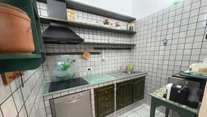 Une cuisine compacte équipée d’un lave-vaisselle, d’un évier et d’une cuisinière. On y trouve des étagères ornées d’objets décoratifs et une petite table avec une bouilloire.