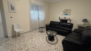 Un salon avec un canapé en cuir noir, un fauteuil blanc, une table basse en verre et un sol carrelé.