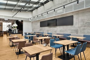Un interior de restaurante moderno con varias zonas de estar, incluyendo mesas y cabinas, y una pantalla grande en la pared.