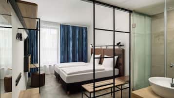 Una camera d'albergo moderna con un letto, un comodino e un bagno con lavandino e doccia.