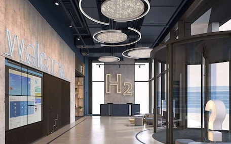 A modern interior with a reception area, a large H2 sign, and a view of the ocean through large windows.