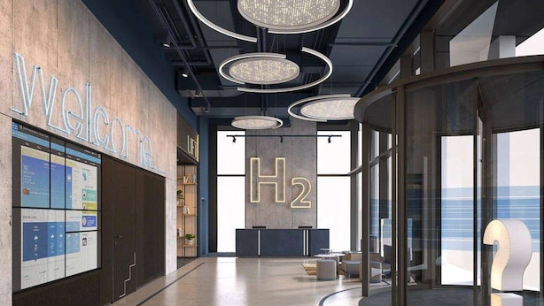 Een modern interieur met een receptiebalie, een groot H2-bord en uitzicht op de oceaan door grote ramen.