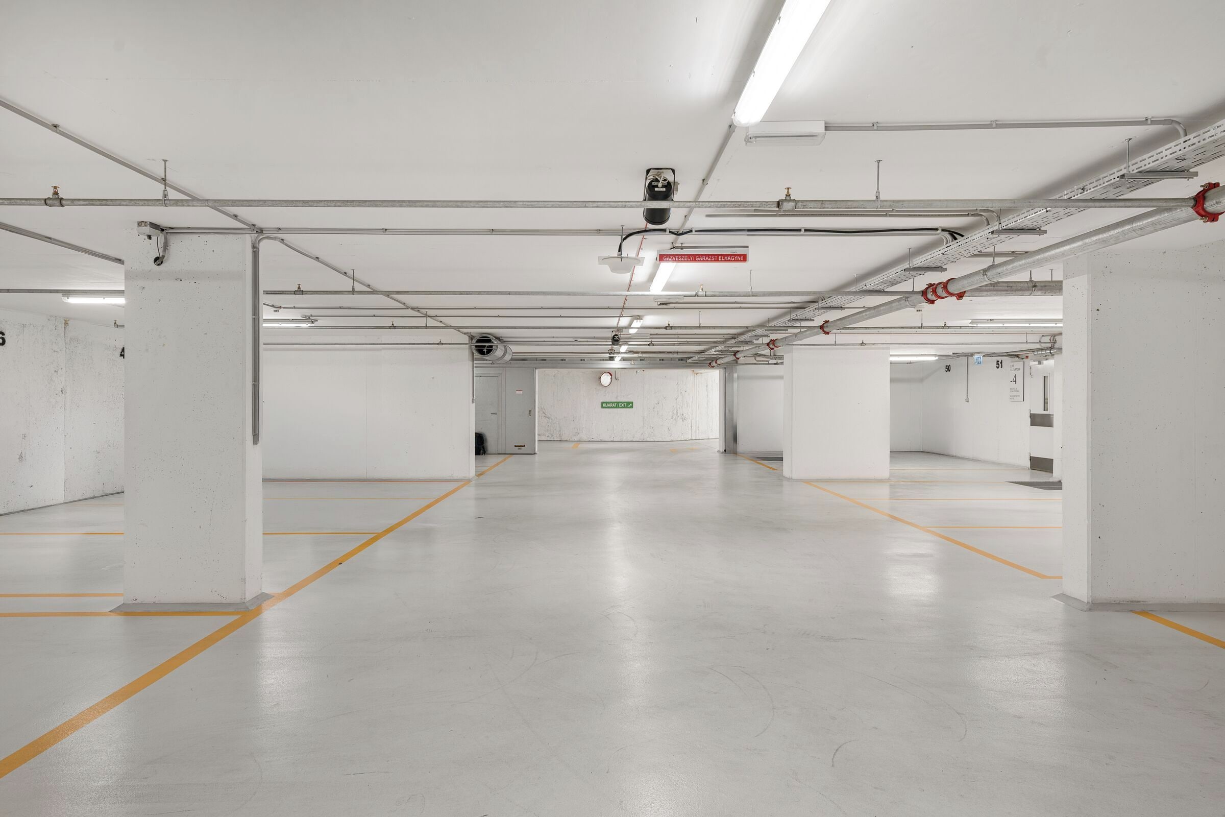 Garagem de estacionamento limpa e vazia, com paredes brancas, pisos de concreto e linhas de demarcação amarela.