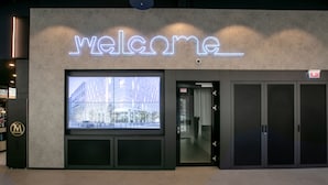 Een modern gebouw met een 'Welcome'-bord en een groot raam dat op een stadsgezicht uitkijkt.