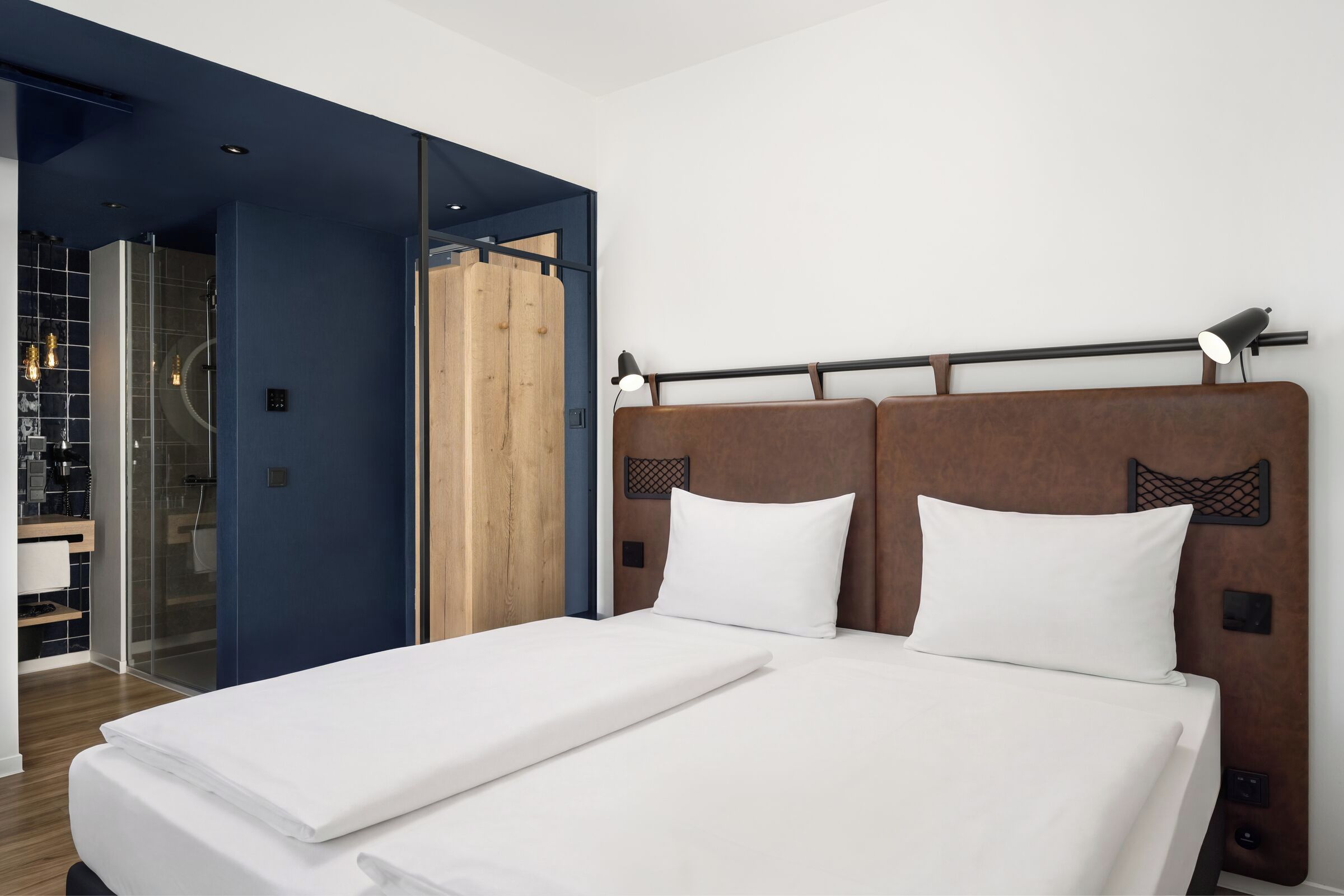 A hotel room with a large bed, a wooden headboard, and a glass shower enclosure.