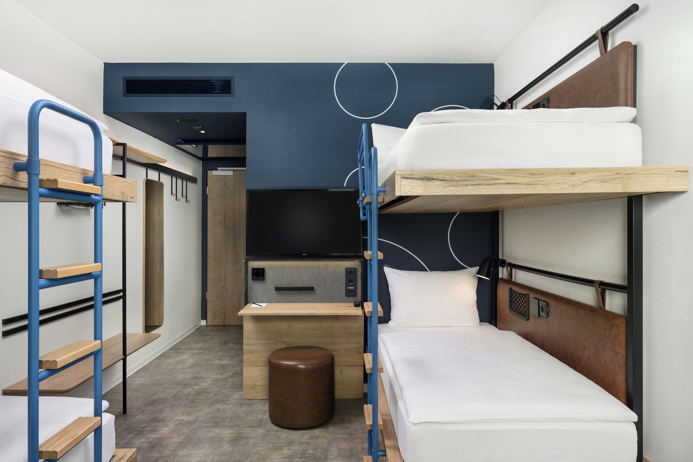 Habitación de hotel compacta con literas, una pequeña mesa de madera, un televisor y un enchufe.