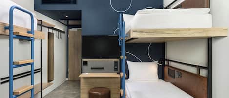 Habitación de hotel compacta con literas, una pequeña mesa de madera, un televisor y un enchufe.