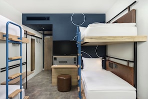 Habitación de hotel compacta con literas, una pequeña mesa de madera, un televisor y un enchufe.
