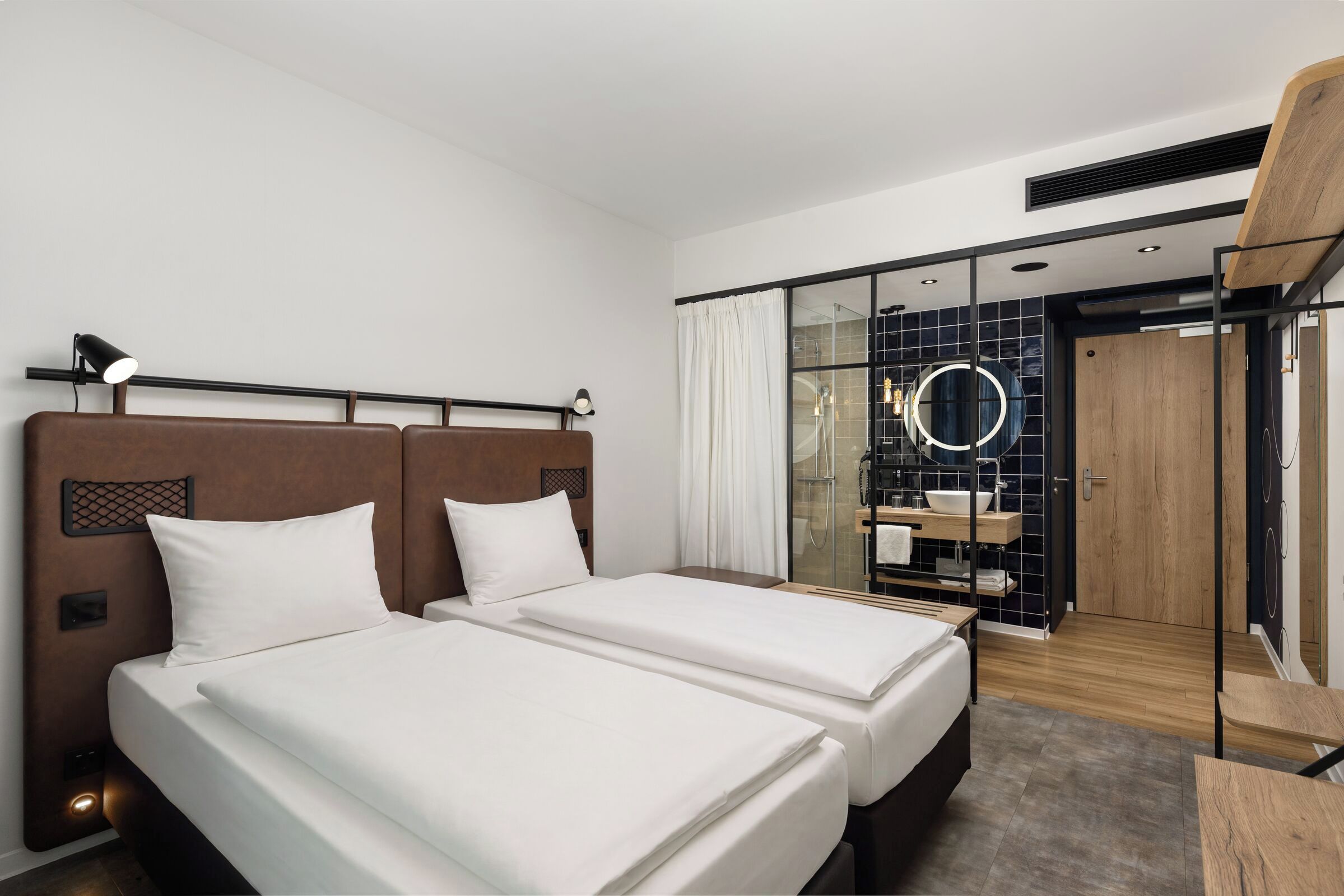 Quarto de hotel com duas camas, um espelho grande, um closet espaçoso e um box de chuveiro.