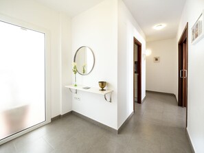 A hallway with a white wall, a mirror, a small shelf with a vase and a bowl, and a door at the end.