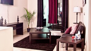Ein modernes Wohnzimmer mit einem Flachbildfernseher, einem dunkelholzigen Couchtisch, einer Topfpflanze, einer Couch mit Kissen und einer Lampe.