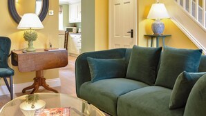A living room with a green sofa, a glass coffee table, a wooden side table, and two lamps.