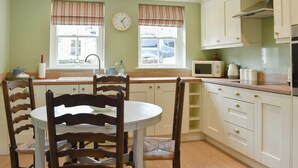 A kitchen with a dining table, chairs, a clock, a microwave, and cabinets.