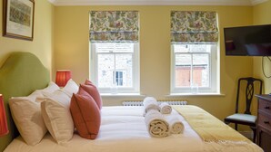 A neatly made bed with pillows, a rolled-up towel, and a bedside table with a lamp.