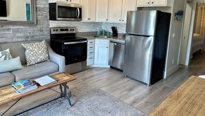 Una cocina moderna con armarios blancos, electrodomésticos de acero inoxidable y un sofá gris con cojines estampados.