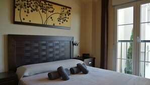 Een opgemaakt bed met kussens, een wandklok en een schilderij erboven.