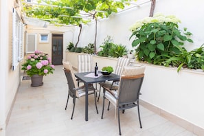 A patio with a table and chairs, surrounded by potted plants and a white wall. - Rooms Batina (Dubrovnik)
