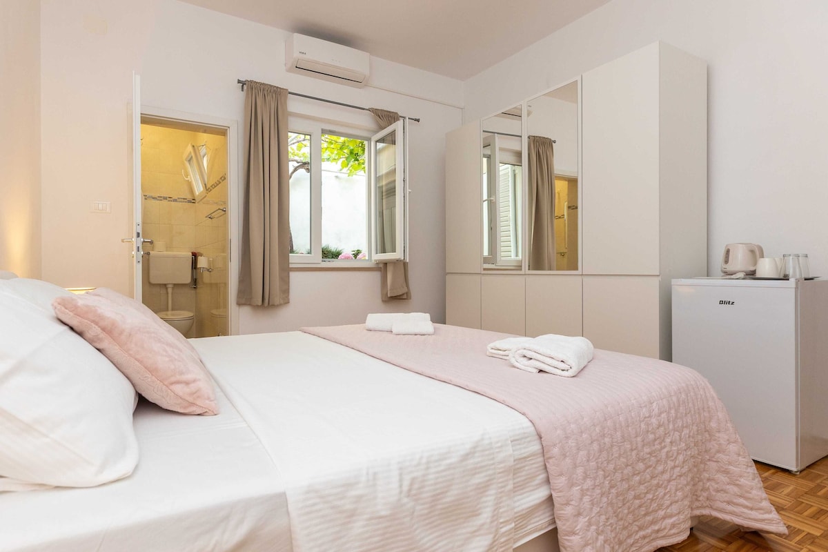 A bedroom with a bed, a wardrobe, a mirror, and a small refrigerator.