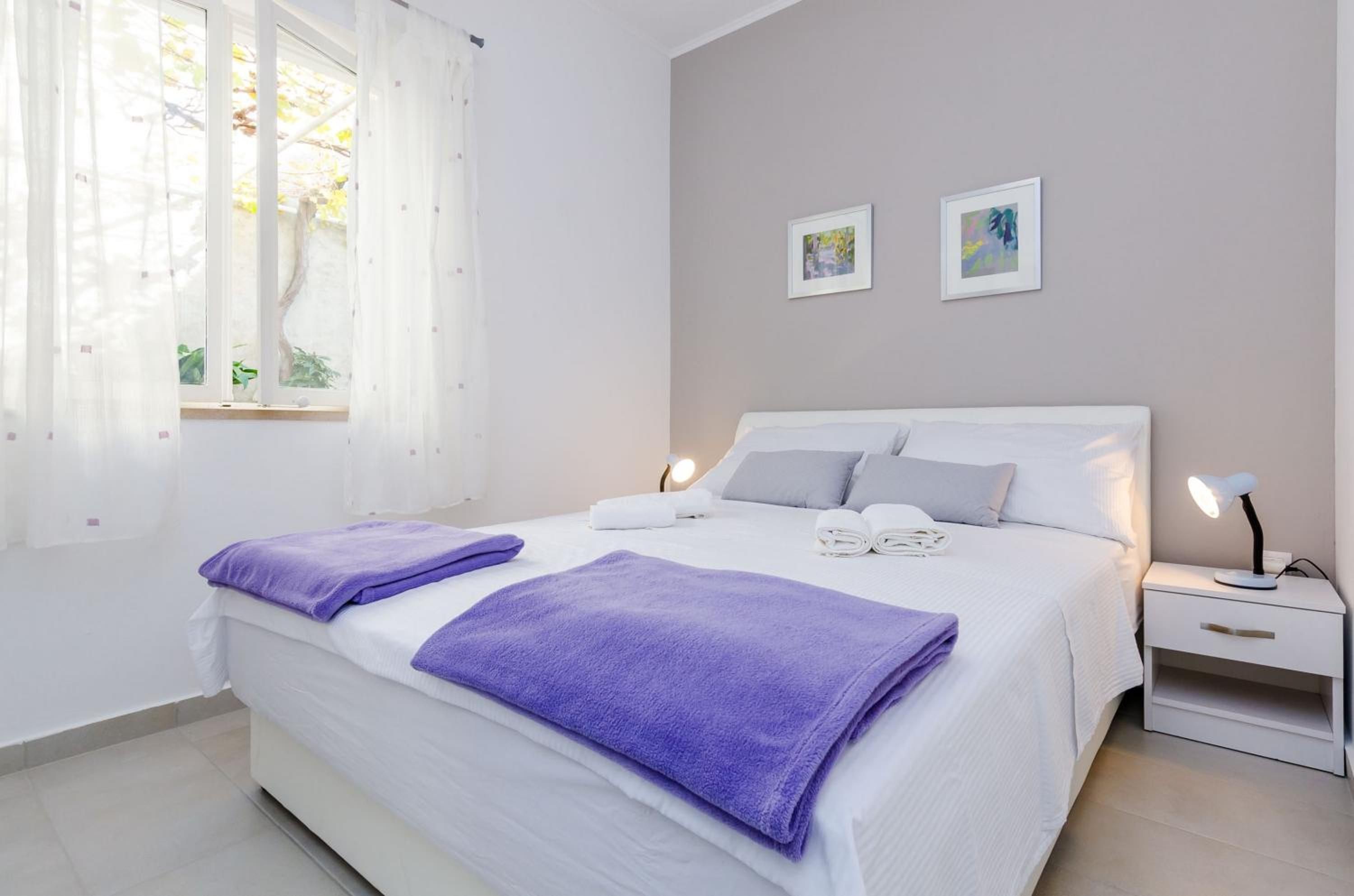 Een slaapkamer met een bed, twee nachtkastjes, een raam met gordijnen en twee aan de muur bevestigde foto's.