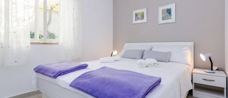 Een slaapkamer met een bed, twee nachtkastjes, een raam met gordijnen en twee aan de muur bevestigde foto's.