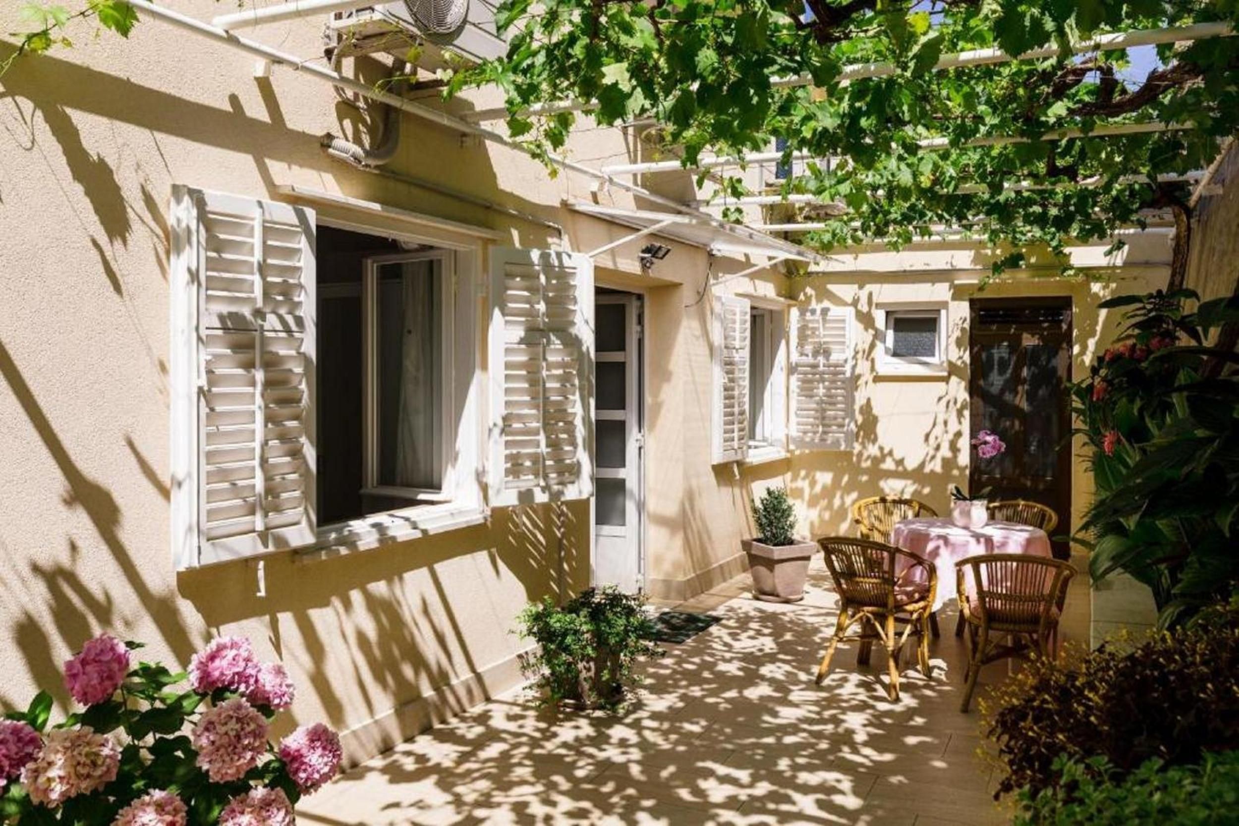 A sunlit courtyard with a table and chairs, a small plant, and a door.