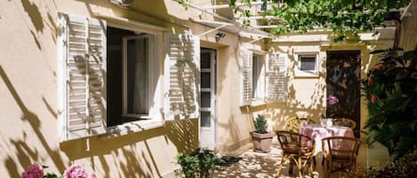 A sunlit courtyard with a table and chairs, a small plant, and a door.