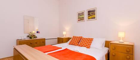 Quarto de hotel com uma cama, duas mesas de cabeceira, um banco de madeira, um espelho e duas molduras na parede.