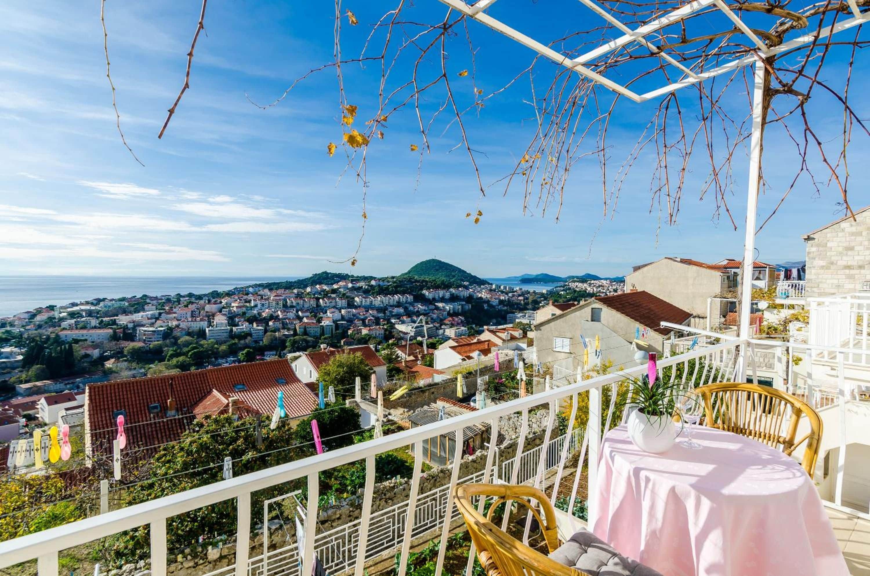 Un balcón con vistas a un pueblo costero, una mesa con mantel y ropa tendida.
