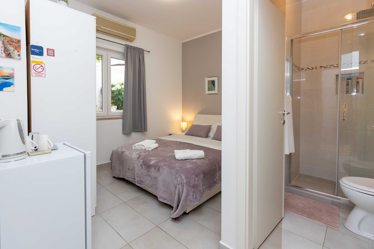 A hotel room with a bed, a bedside table with a kettle, a shower area, and a toilet.